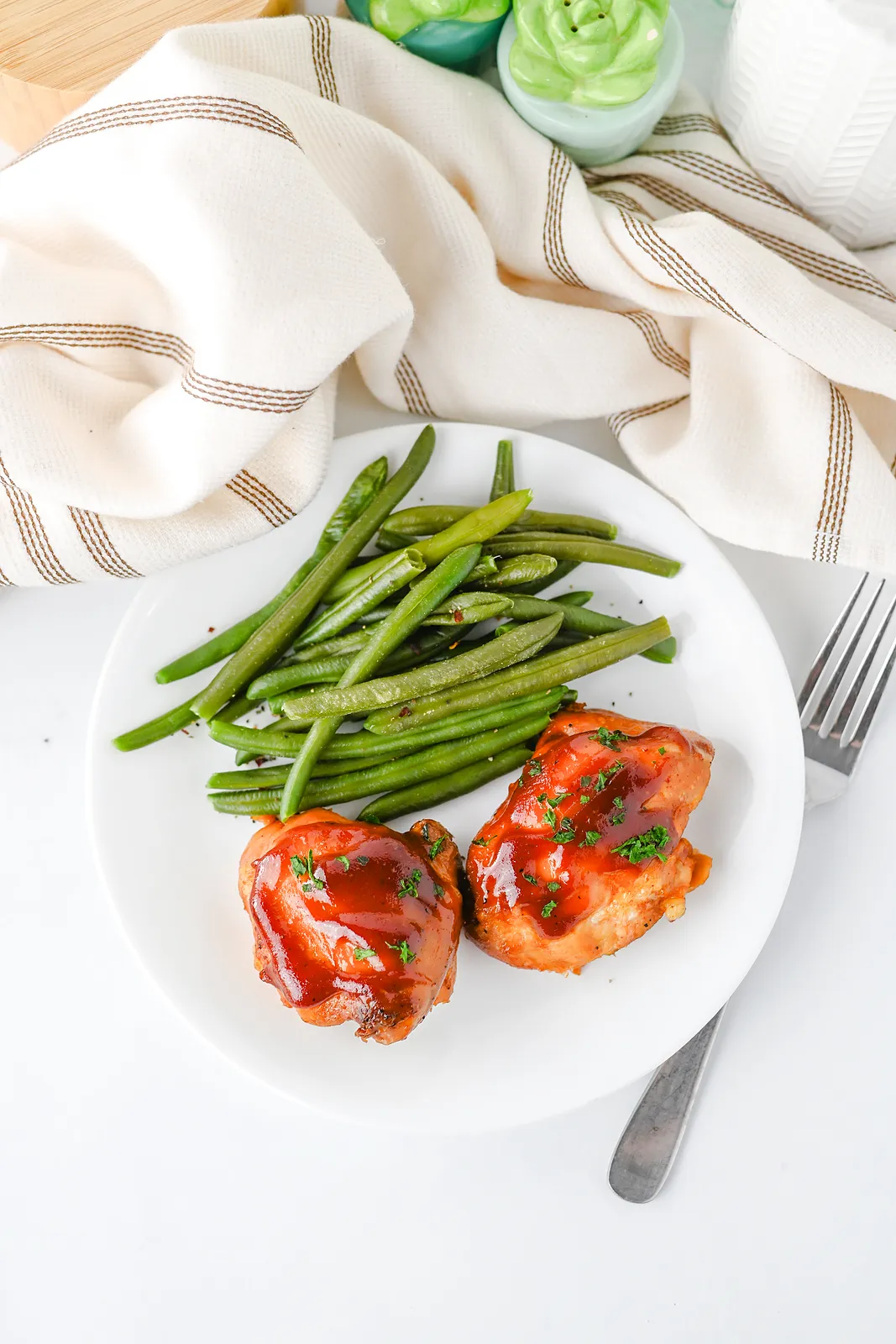 A white plate of sticky glazed pieces and green beans beside a striped tea towel