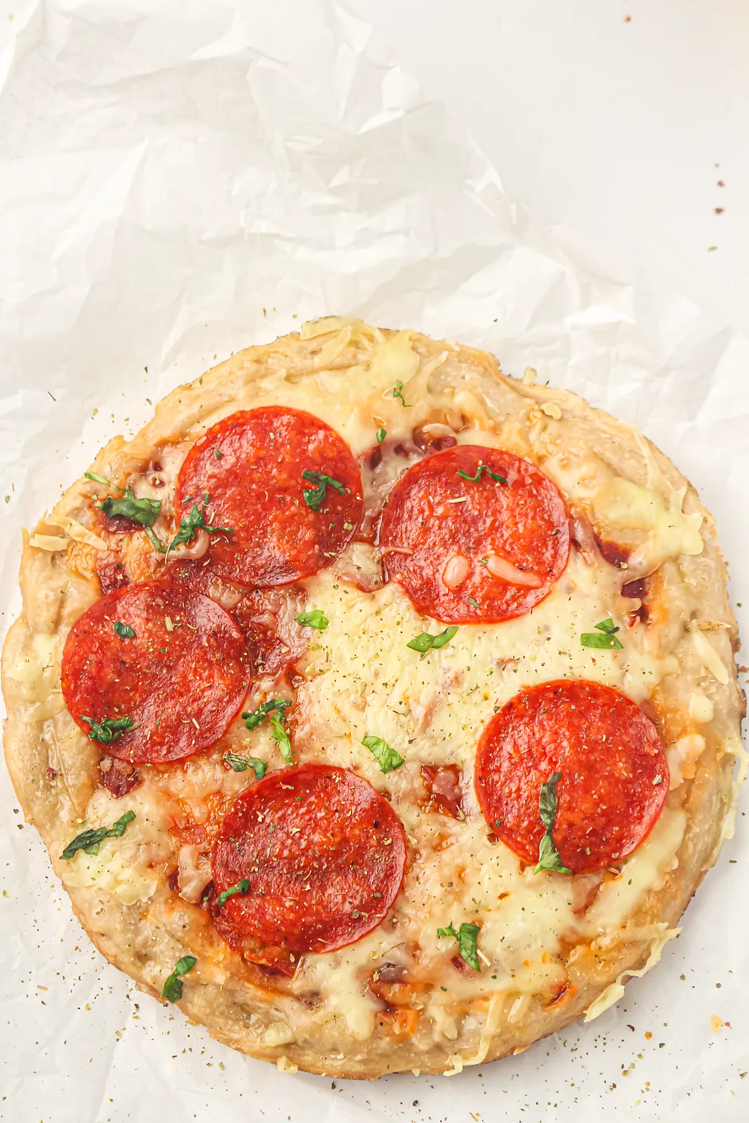 A whole pepperoni pie on crinkled parchment paper with herbs sprinkled over